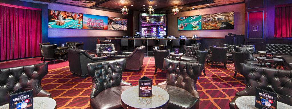Lounge with leather chairs, small tables, and large screens displaying casino games and hotel ads at the Parlour Bar.