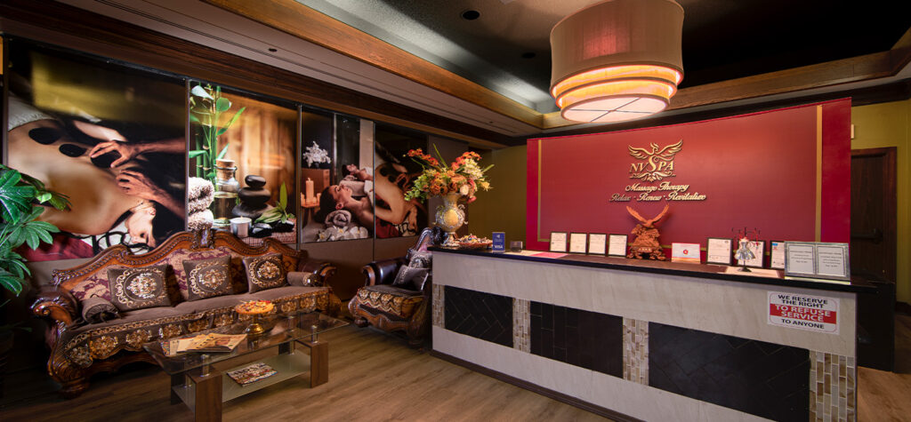 Elegant nv spa reception area with an ornate sofa, large chandelier, and a front desk featuring decorative displays.