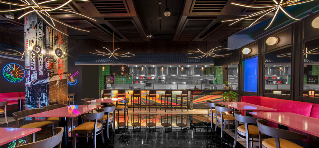 A modern, colorful restaurant with pink tables, wooden chairs, and artistic lighting fixtures.